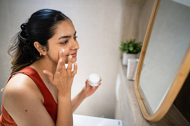 Young Indian woman applying a face cream in front of the mirror.